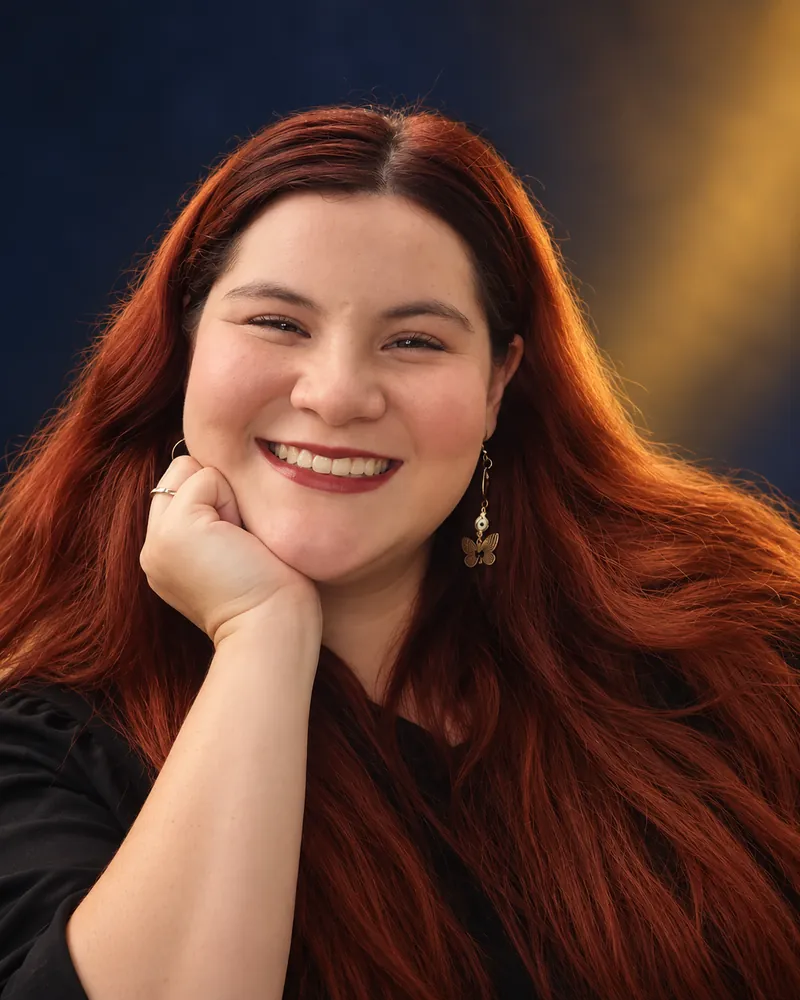 Retrato de estudio de Paola Muñoz sonriendo, con la mano bajo el mentón